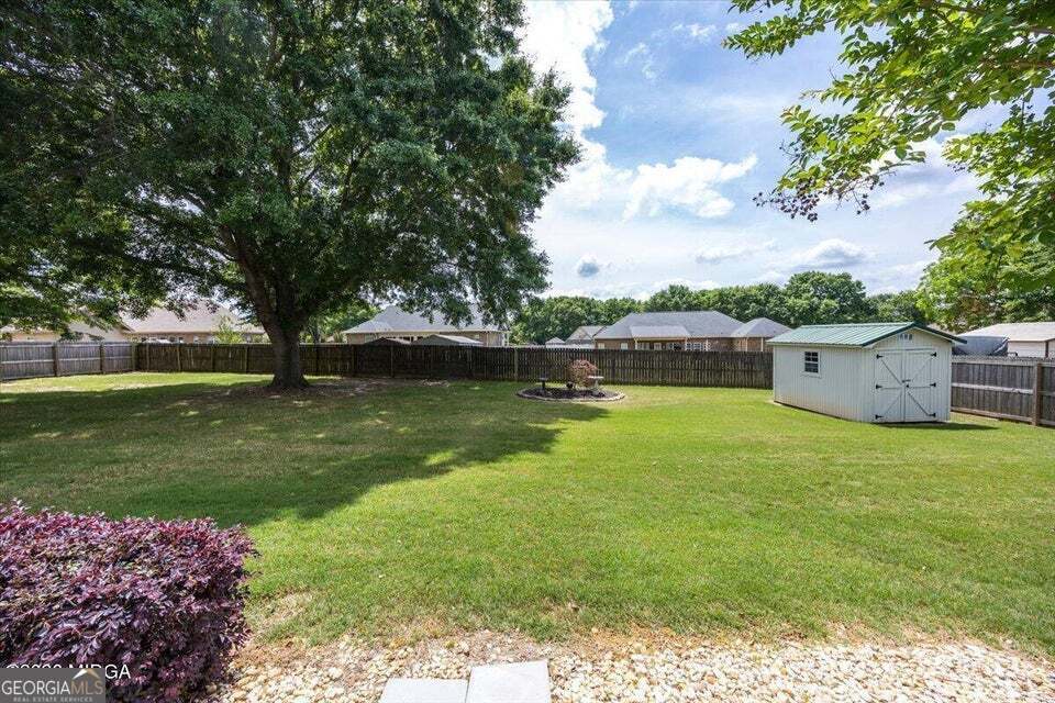 Spacious backyard at 411 Dixieland Drive in Byron GA featuring mature shade tree, storage shed, and large private outdoor space in Peach County