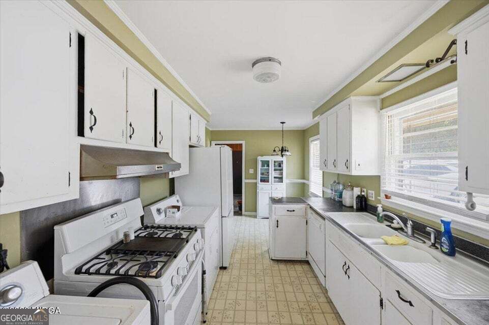 Bright galley-style kitchen at 2418 Tredway Drive in Macon, Georgia featuring extensive white cabinetry, double sink, natural light, eat-in layout, gas stove, and functional workspace with vintage character.