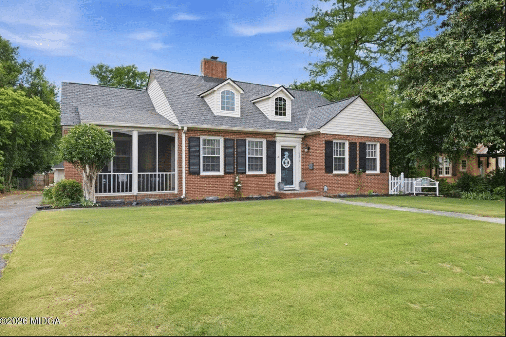 Brick ranch-style house with a large front lawn, black shutters, and a screened porch on the left; two dormer windows above the front door with wreaths on the blue door.