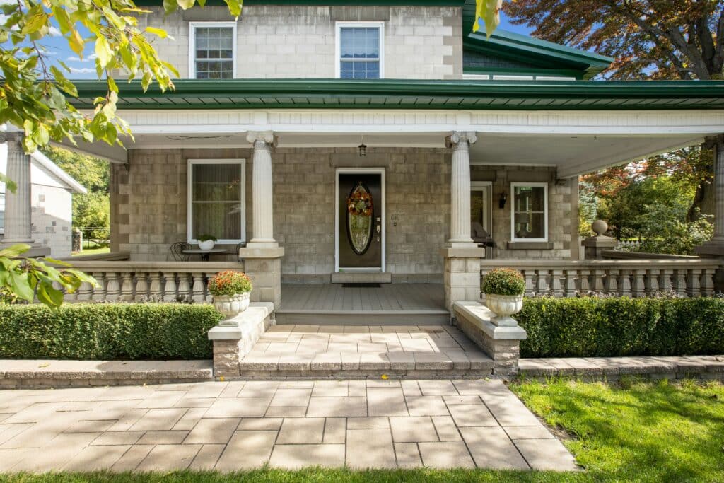 Front view of a stone house with a covered porch, two columns, and a wreath on the oval front door.