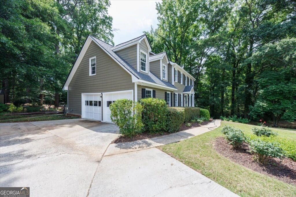Side exterior view of 1301 Craddock Way in Rivoli Lakes, featuring a traditional two-story home with a two-car garage, mature landscaping, and a wooded North Macon setting.