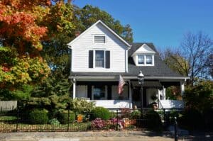 Traditional white two story home with a covered front porch, black shutters, manicured landscaping, and vibrant autumn trees, representing an attractive residential investment property.