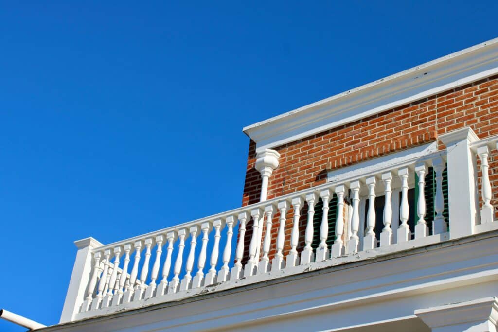 Historic brick home with white balcony railing showcasing classic architectural details and curb appeal