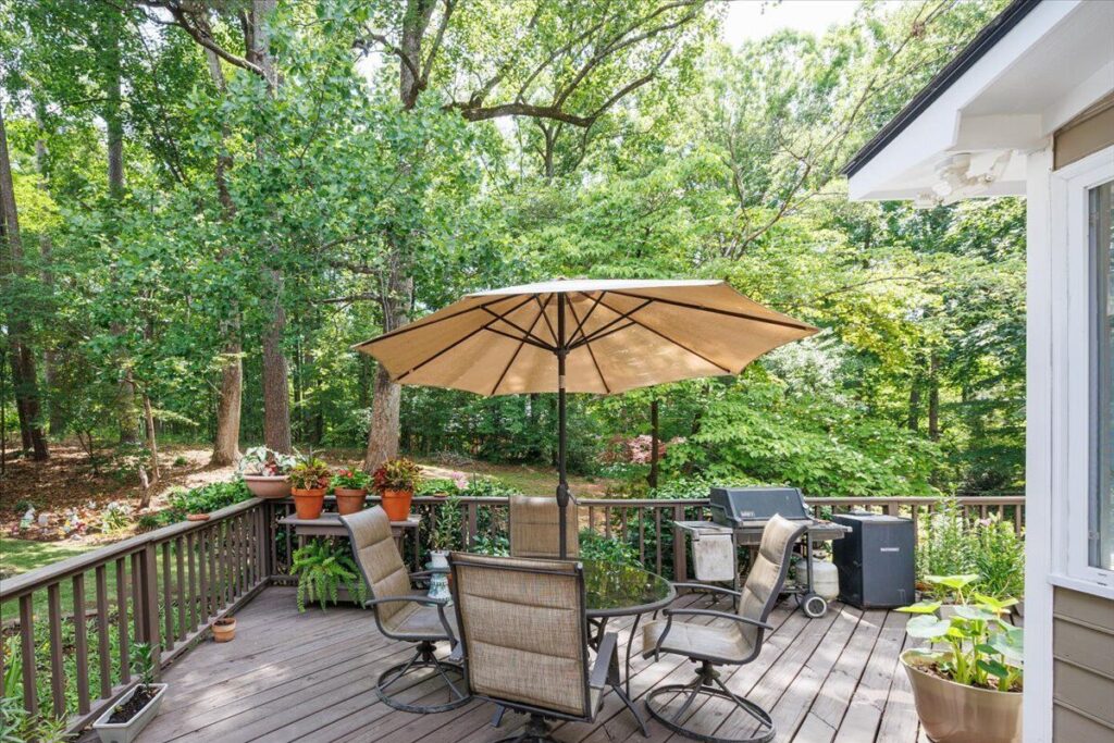 1301 Craddock Way Backyard Deck in North Macon - Patti Chapman Real Estate™ Backyard deck with outdoor dining table, umbrella and wooded surroundings at 1301 Craddock Way in Macon, GA.