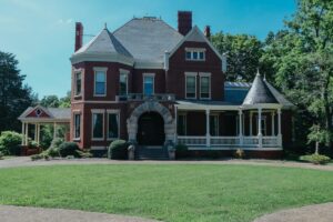 Historic red brick Victorian home with turret, wraparound porch, and mature landscaping